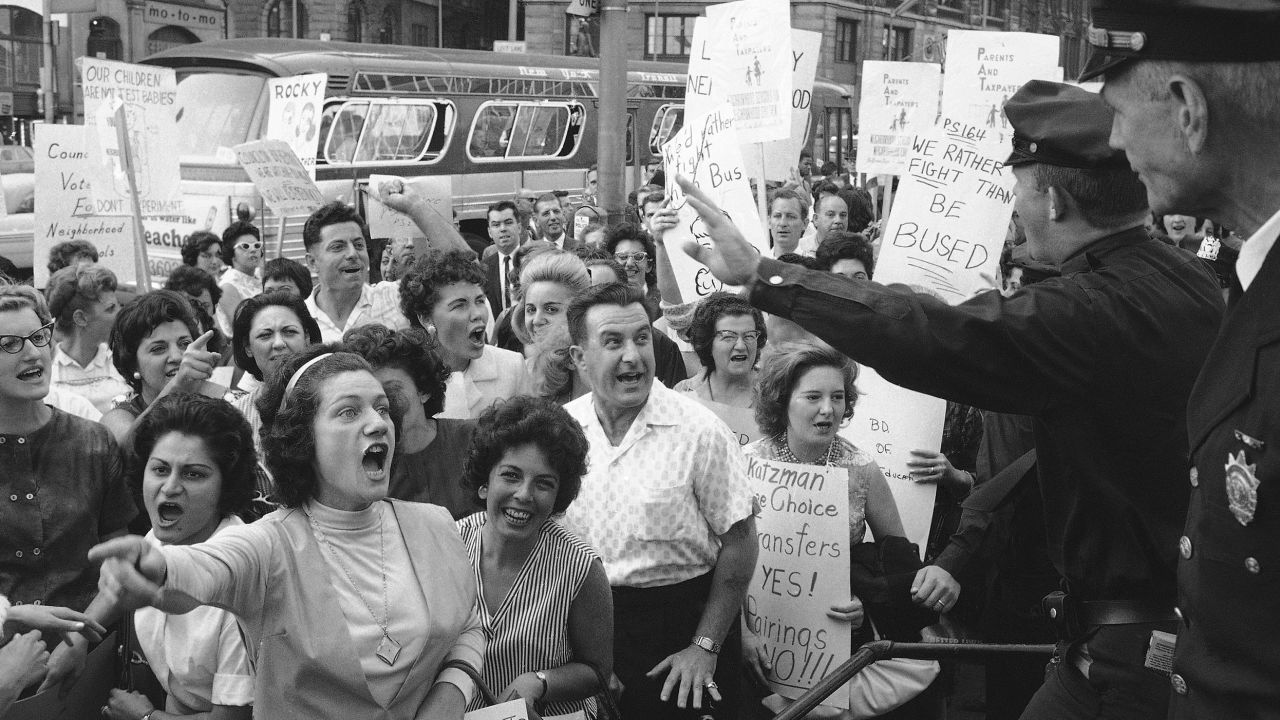 Demonstrators shout at policemen who ask them to move on along City Hall in New York, Sept. 24, 1964 as they protest a Board of Education busing program aimed at increasing racial balance in New York City schools. A city council meeting discussing the program in City Hall later defeated a motion to take to the floor a resolution calling for a referendum on busing. (AP Photo/Harry Harris)